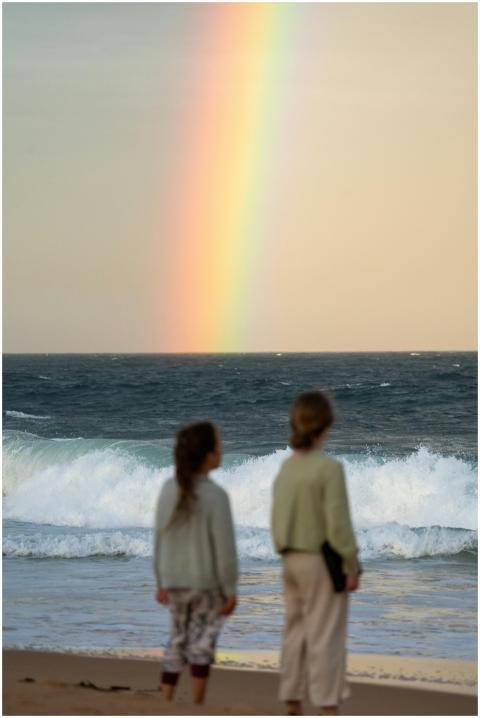 Two children watching a rainbow over the ocean wav