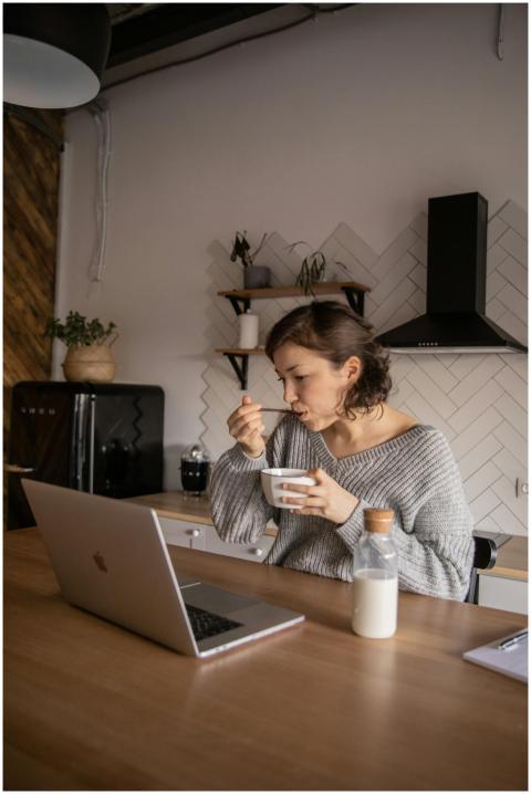 Female enjoys breakfast while browsing on a laptop