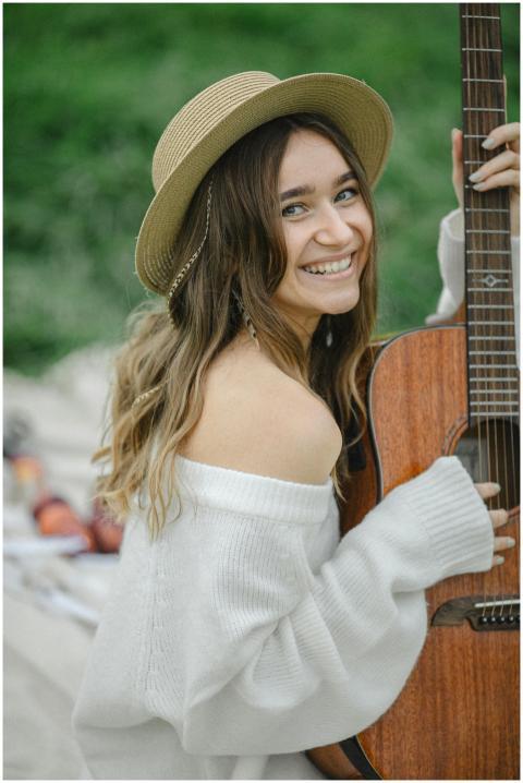 Smiling woman in a hat holding a guitar outdoors i