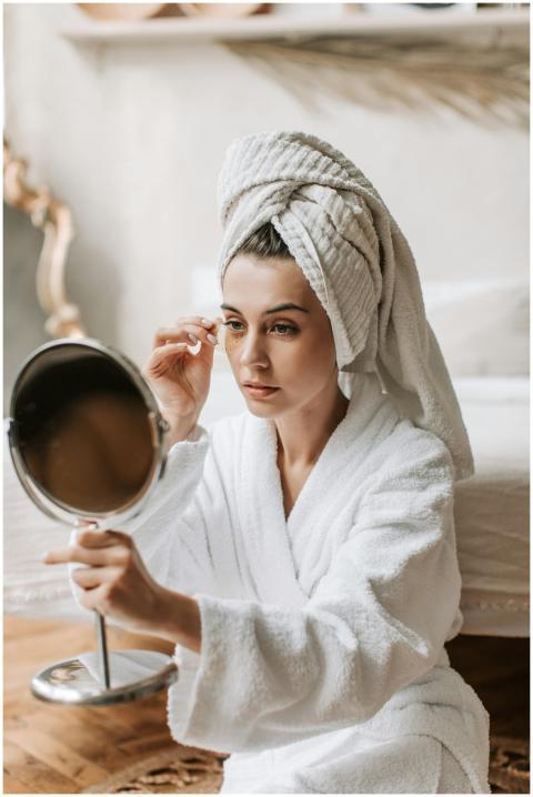 Woman in a bathrobe applying makeup in front of a