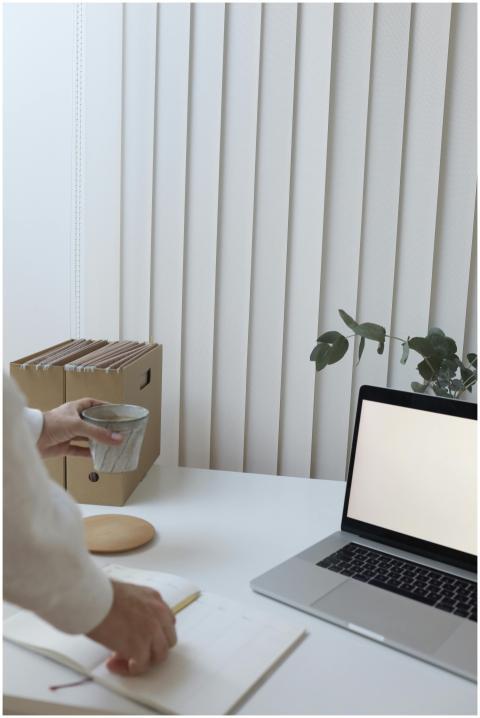 Crop faceless person standing near table with lapt