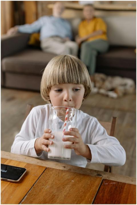 A young boy drinks milk with a straw while grandpa