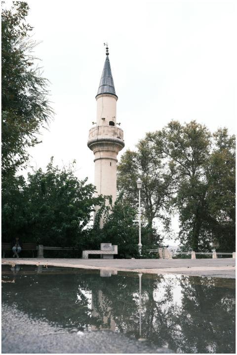 A historic minaret is reflected in a puddle surrou