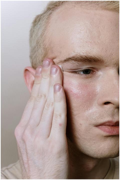 A young man applying skincare product to his cheek