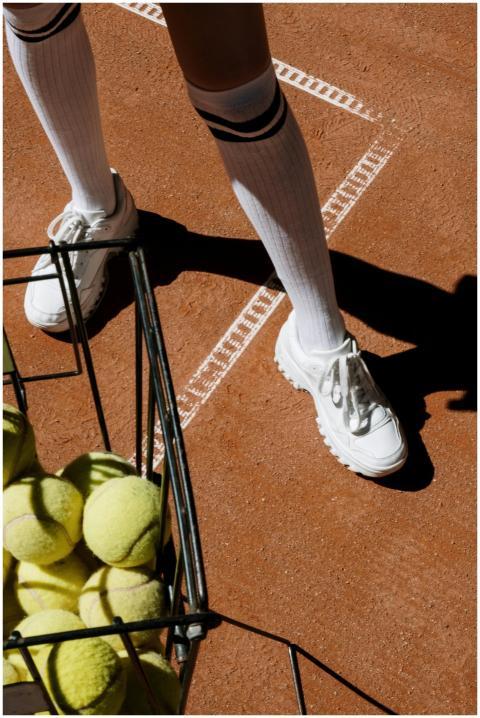 Close-up of tennis shoes and ball basket on a clay