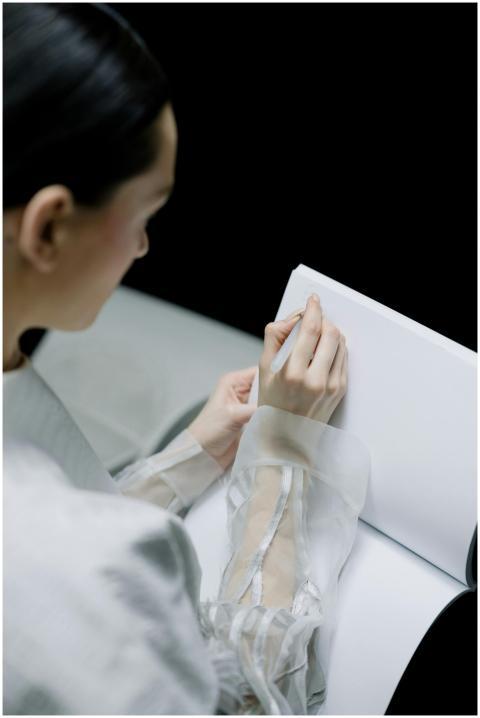 A woman writing on a large white notebook viewed f