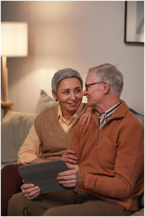 Happy elderly couple sitting on sofa, using tablet