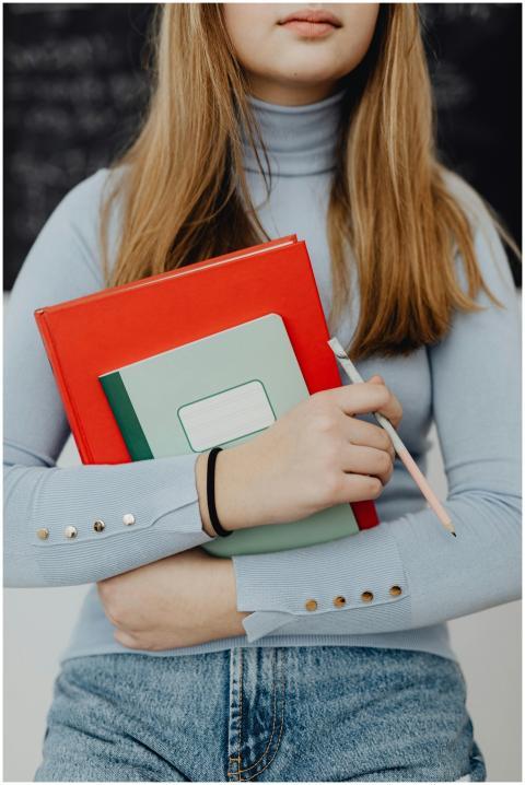 Teenage girl holding textbooks and a pen in a clas