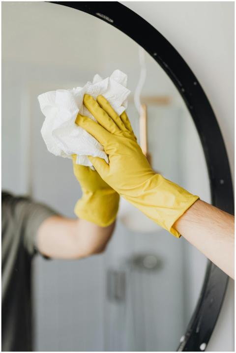Close-up of a person cleaning a mirror with yellow