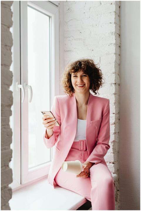 Brunette woman in a pink suit sitting by a window,