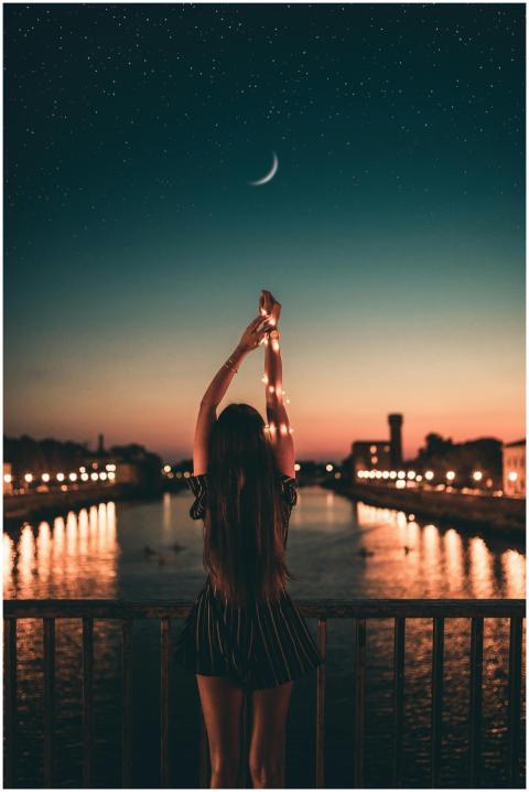 A woman stands with arms raised, gazing at a starr