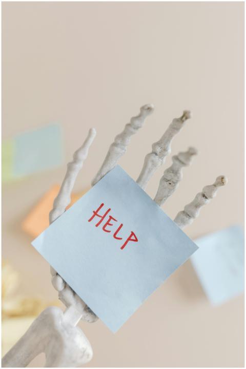 Skeleton hand holding a note with 'HELP' written,