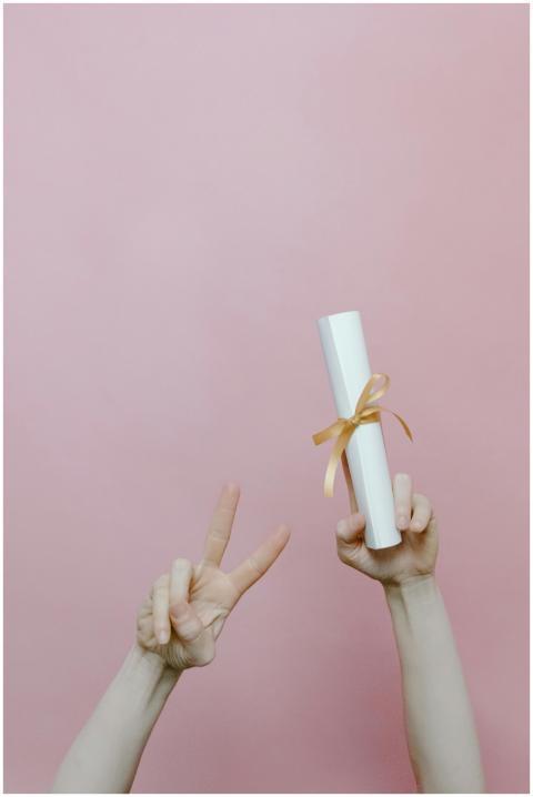 Diploma held in hand with peace sign on pastel pin