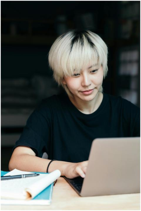 Cheerful young Asian woman browsing laptop indoors
