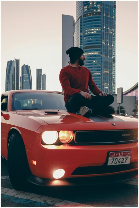 A man sitting on a Dodge Challenger at twilight wi
