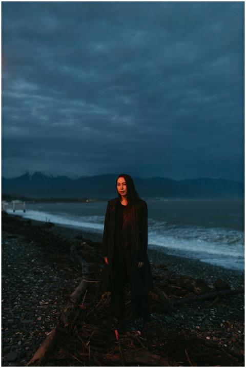 A mysterious woman stands on a rocky shoreline by