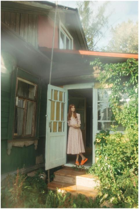 A young woman in a vintage dress stands at the ent