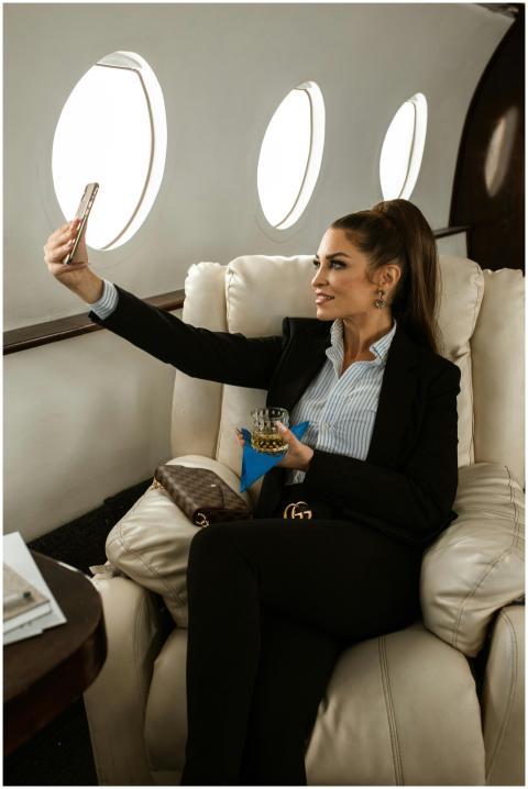 Elegant woman in blazer sits in airplane, taking s