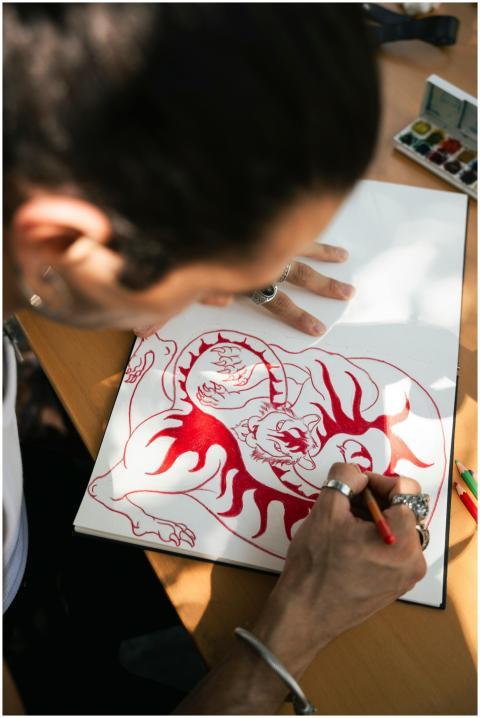 An artist sketching an intricate red dragon tattoo