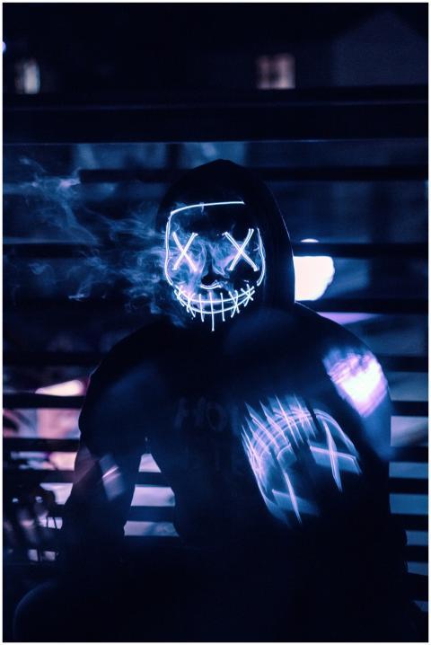 A mysterious figure in a neon mask and hoodie capt