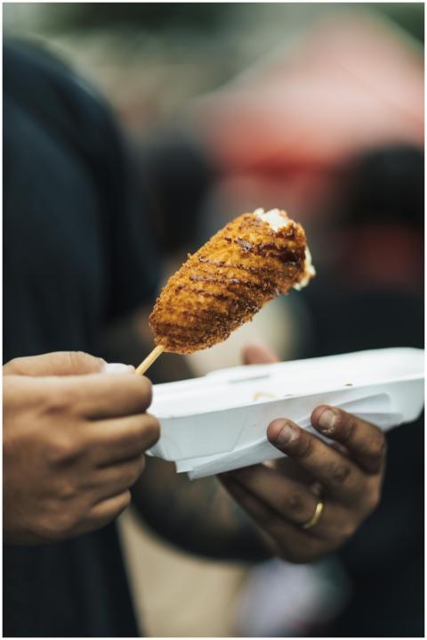 Man holding a crispy fried corn dog in a paper tra