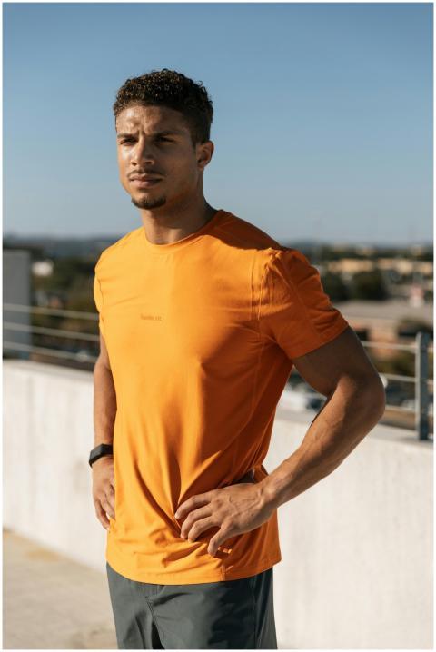 Fit man in orange shirt poses confidently on rooft