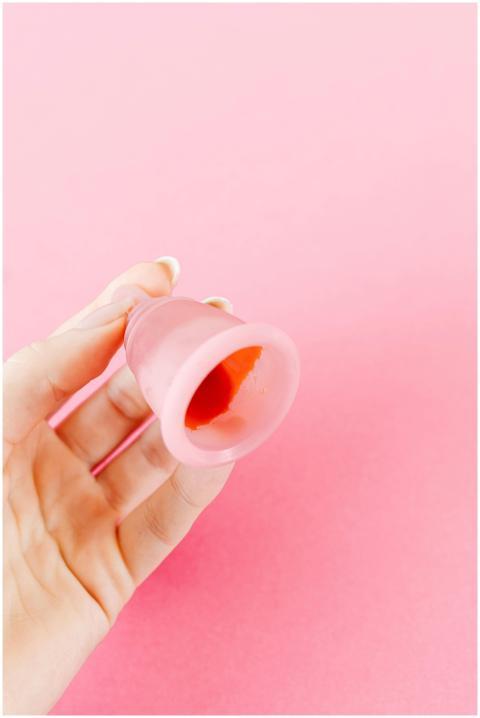 A close-up of a hand holding a pink menstrual cup