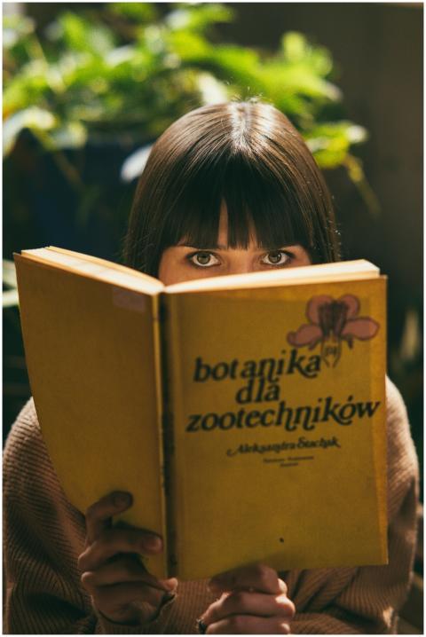A young woman with bangs reads a botanical book in