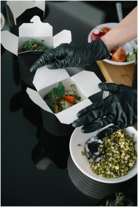 Gloved hands preparing fresh salad takeout in eco-