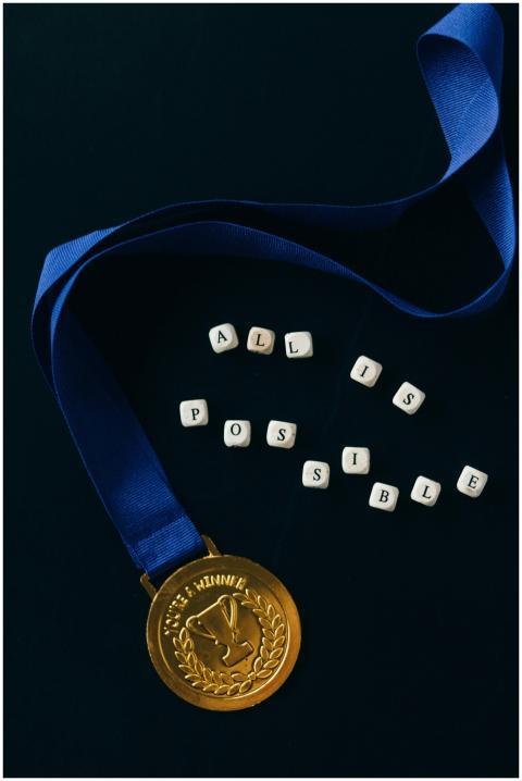 A gold medal with a blue ribbon and 'All is Possib