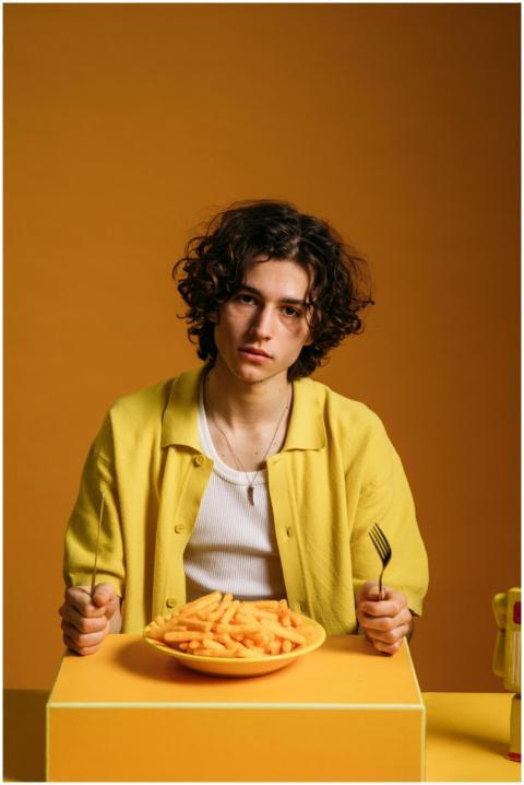 Young man with curly hair eating fries, set agains