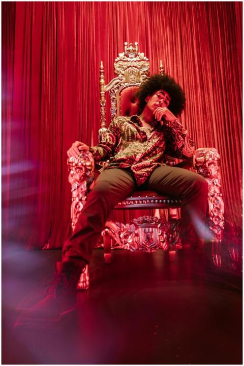 A fashionable man confidently sits on a lavish thr