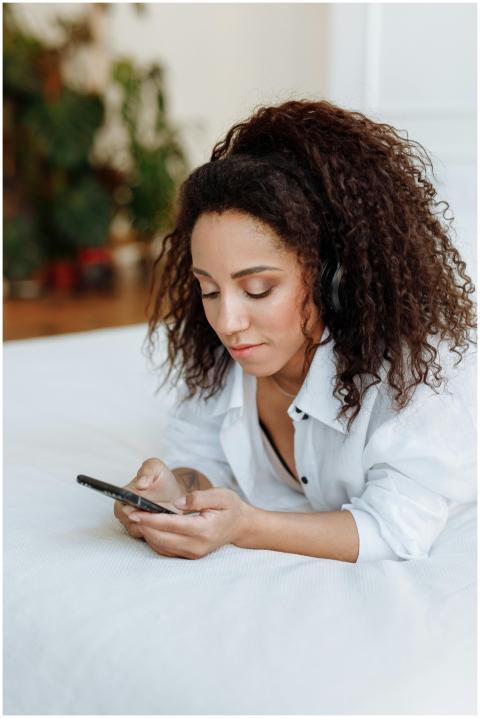 Woman lying on bed with headphones, using smartpho