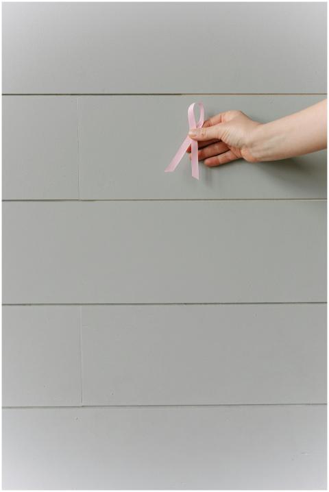 A hand holding a pink ribbon against a neutral bac