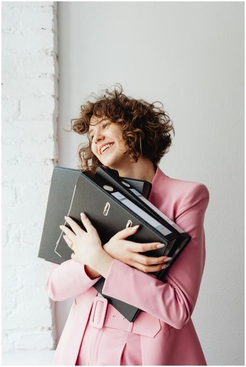 Cheerful woman embracing binders, wearing a pink b