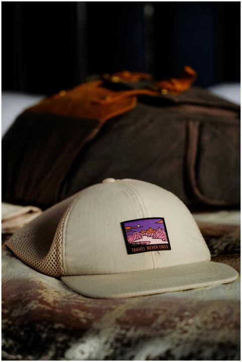 Beige mesh cap with 'Travel Never Ends' patch on a