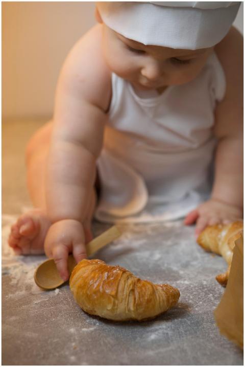 Cute baby in chef outfit playing with croissant on