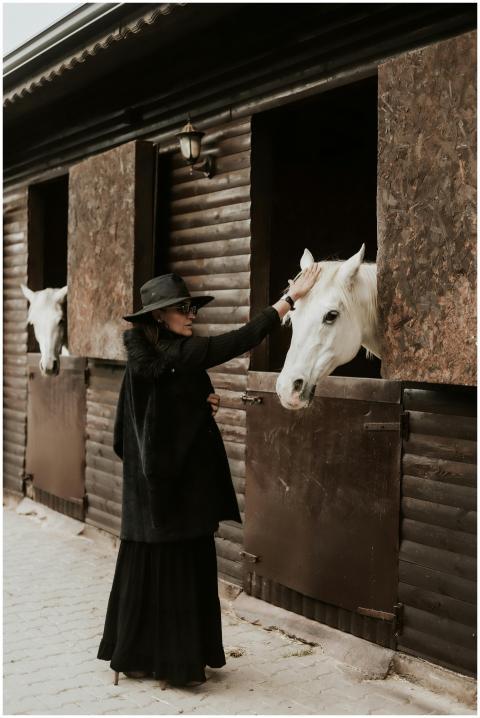 Stylish woman in a hat lovingly pets white horses