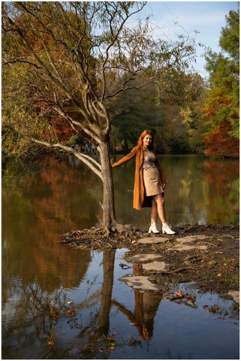 A woman with red hair standing by a pond reflects