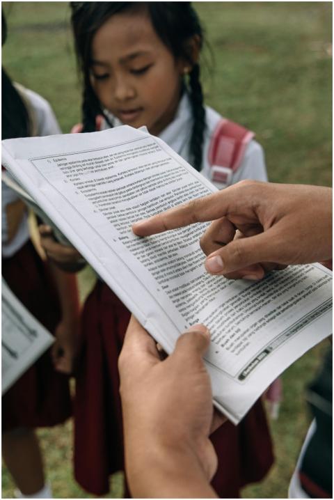 A teacher shows text in a book to students in scho