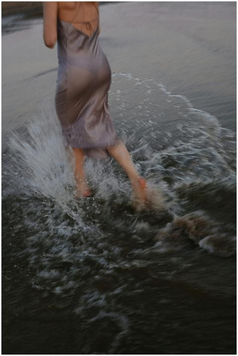 A woman in a dress splashes through the shallow wa