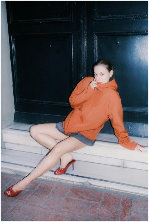 Stylish woman in an orange hoodie sitting on steps