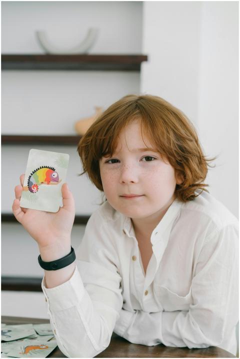 Child in white shirt holding a colorful card indoo