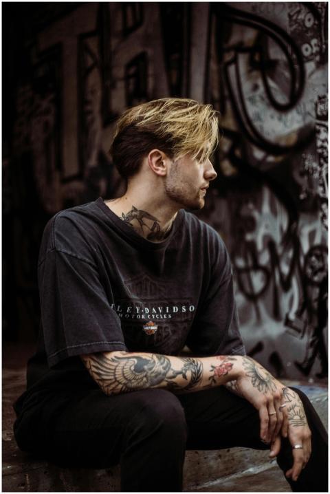 A tattooed man in a black T-shirt sits in a graffi