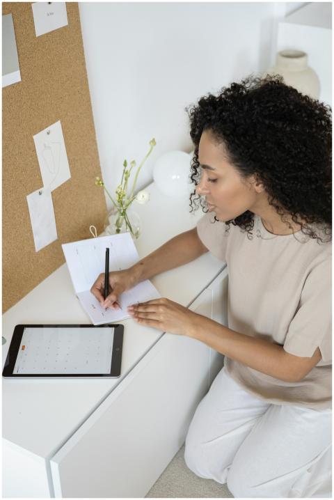 A young woman with curly hair writes notes in a mo