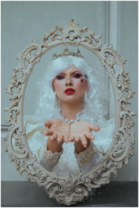 A regal woman in a white dress and crown posed ele