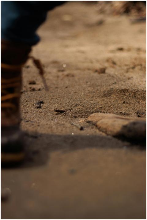 A detailed close-up of boots on a sandy path, show