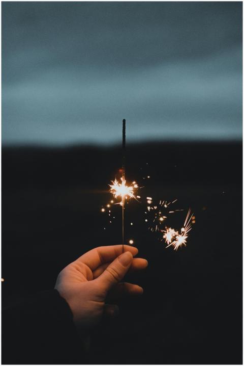 A sparkler brightens a dark night held by a hand,