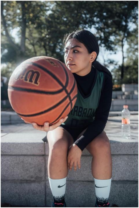 A young female basketball player sits outdoors hol