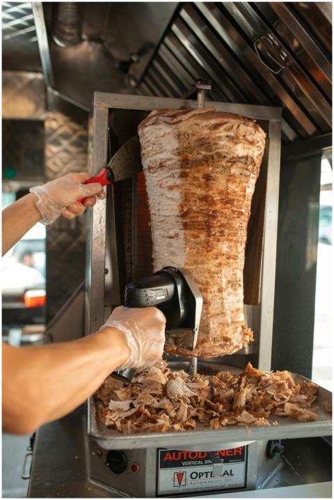 Hands slicing shawarma meat on a vertical rotisser
